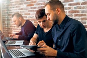 Profissionais analisando informações em frente a computadores em um coworking para empresas de TI.