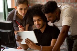 Três profissionais de TI analisando informações no tablet, representando o avanço tecnológico decorrente da redução de ISS.