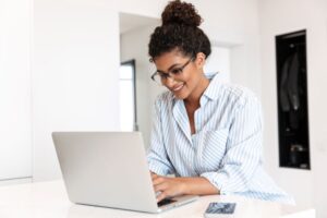 mulher sorridente trabalhando no computador na cozinha de sua casa