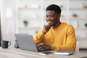 Homem sorridente em escritório verificando sua agenda profissional no notebook.