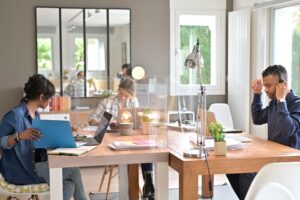 Saúde e qualidade de vida: pessoas trabalhando em coworking em conjunto de mesas em formato de ilha.