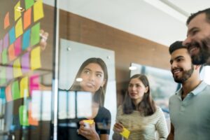 Tipos de inovação: equipe no coworking por trás de vidro analisando ideias em post-its.