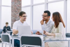 Escritório compartilhado​: três colegas trabalhando e conversando em mesa de coworking.
