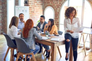 economia colaborativa​: mulher encostada em mesa onde equipe está reunida em coworking