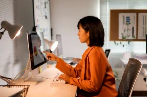Empresária asiática analisando dados e gráficos no computador em escritório sobre o que é margem de contribuição.